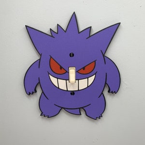 May include: Purple and black light switch cover featuring a cartoon illustration of a Ghost-type Pokemon with a wide, toothy grin.