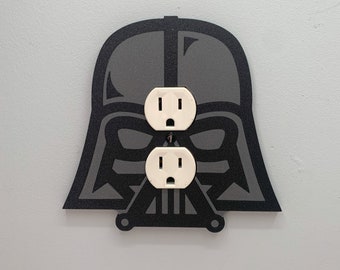 May include: A black and gray Darth Vader-themed wall plate with two white electrical outlets.