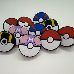 Puede incluir: Una colecci&oacute;n de dise&ntilde;os redondos y coloridos de estilo caricatura que se asemejan a Pok&eacute; Balls. Los dise&ntilde;os presentan varios esquemas de color, incluyendo rojo y blanco, azul y blanco, y morado con acentos rosas. Algunos tienen una "M".