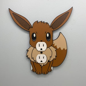 May include: A brown and tan Eevee Pokemon wall plate cover with two standard electrical outlets.