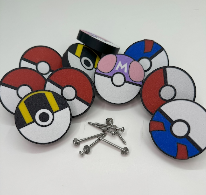 Puede incluir: Una colecci&oacute;n de pomos de armario redondos y coloridos con varios dise&ntilde;os, incluyendo rojo y blanco, negro y amarillo, y morado con la letra "M". Tambi&eacute;n se ven varios tornillos plateados, lo que sugiere que est&aacute;n listos para la instalaci&oacute;n.