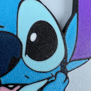 May include: Close-up of a blue and purple cartoon character with one large black eye and a white highlight. The character has a textured surface.