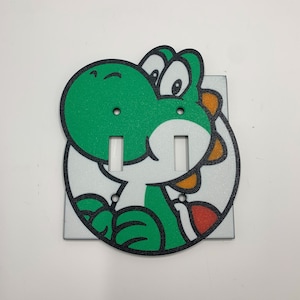 May include: A green and orange light switch cover featuring a cartoon Yoshi character from the Super Mario video game series.