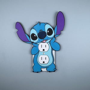 以下が含まれることがあります： 青い紫色のスティッチのキャラクターのライトスイッチカバーで、標準の米国電気コンセントが2つあります