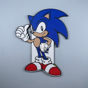 May include: A blue and red light switch cover featuring a cartoon character of Sonic the Hedgehog giving a thumbs up.
