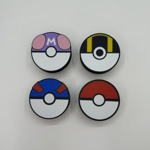 Puede incluir: Cuatro dise&ntilde;os circulares y coloridos que se asemejan a Pok&eacute; Balls. Cada bola presenta una mitad inferior blanca y un borde negro. Las mitades superiores son moradas con acentos rosas y una "M" blanca, negras con acentos amarillos, azules con acentos rojos y rojas s&oacute;lidas.