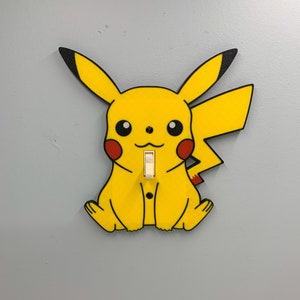 May include: A yellow Pikachu light switch cover with black outlines and red cheeks. The switch is white and has the word "ON" printed on it.