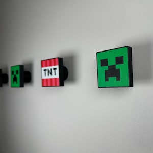 May include: Four wall-mounted Minecraft-themed decorations. The decorations are made of wood and feature a green creeper face, a red and white TNT block, a green creeper face, and a green creeper face.