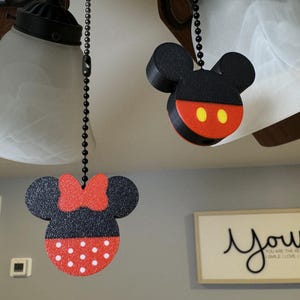 May include: Two black and red fan pull chains with a Mickey Mouse and Minnie Mouse design. The Mickey Mouse pull chain has yellow circles for eyes. The Minnie Mouse pull chain has a red bow and white polka dots.