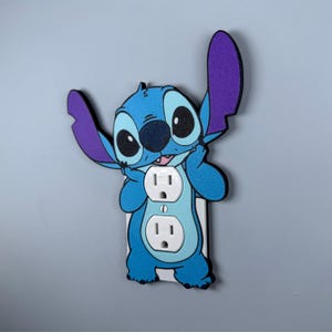 May include: A blue and purple Stitch character wall plate cover for a standard US electrical outlet.