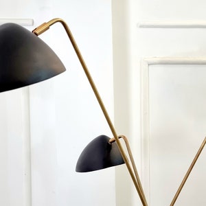 May include: A gold floor lamp with three black shades. The lamp has a modern design with a long, slender stem and three adjustable arms.