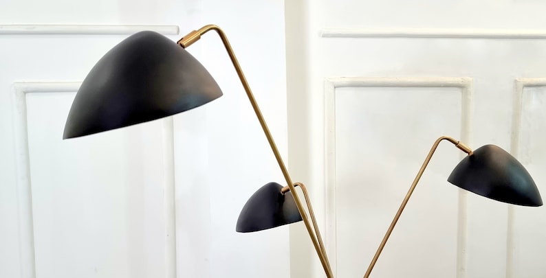 May include: A gold floor lamp with three black shades. The lamp has a modern design with a long, slender stem and three adjustable arms.
