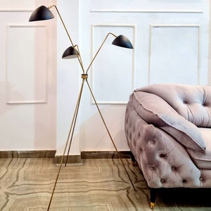 May include: A gold tripod floor lamp with three black lampshades. The lamp is in a room with white walls and a light pink sofa.