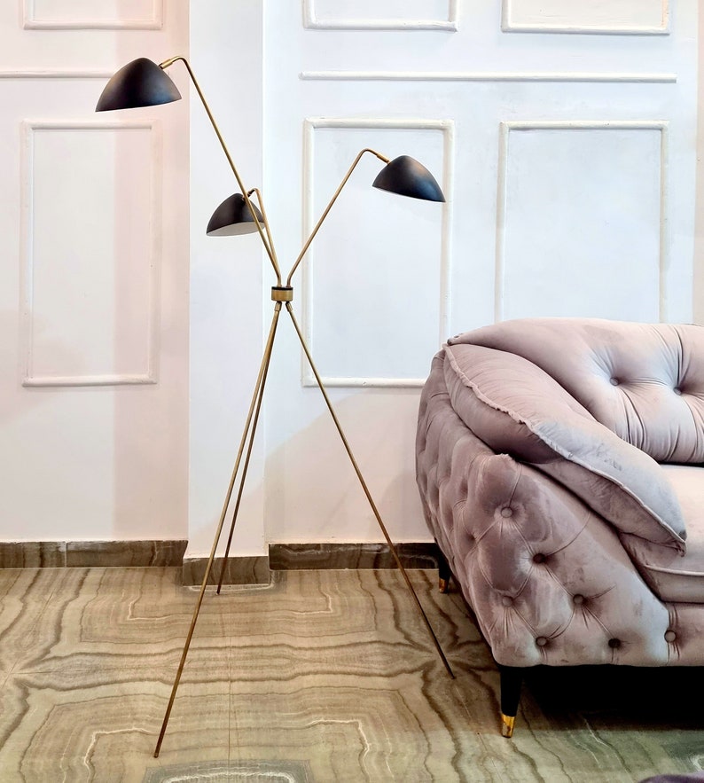 May include: A gold tripod floor lamp with three black lampshades. The lamp is in a room with white walls and a light pink sofa.
