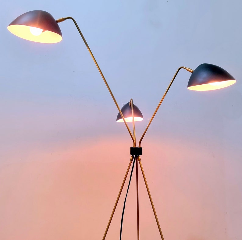 May include: A gold floor lamp with three black lampshades. The lamp has a tripod base and adjustable arms.