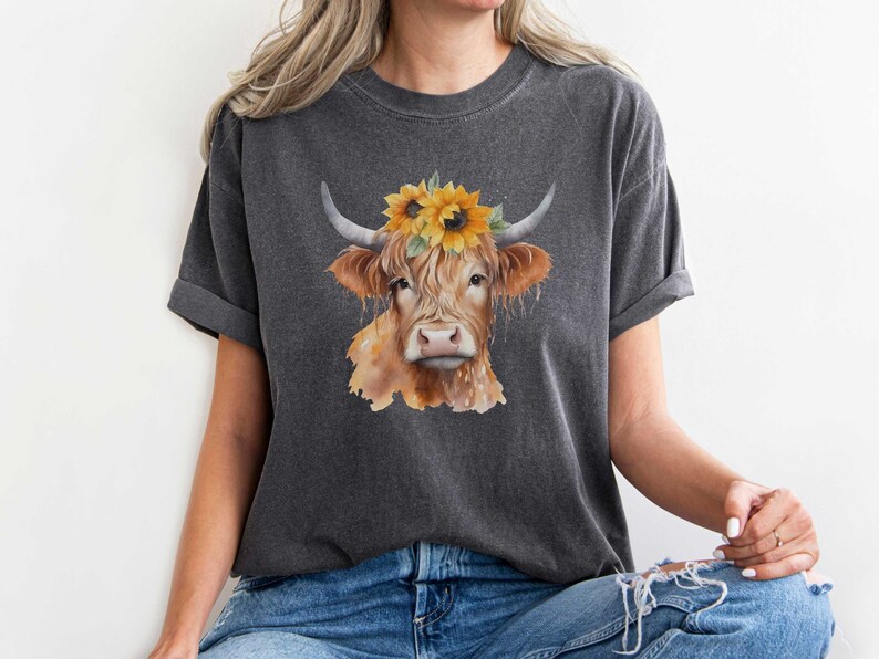 May include: A gray t-shirt with a watercolor illustration of a brown and white cow wearing a sunflower crown.