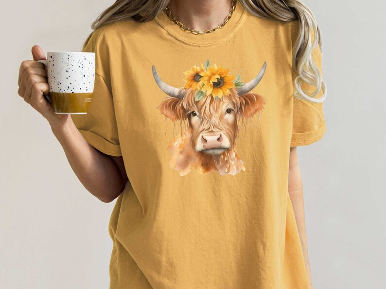 May include: A yellow t-shirt with a watercolor illustration of a brown Highland cow wearing a sunflower crown.