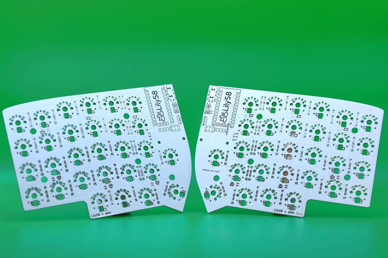 Peut inclure: Deux circuits imprim&eacute;s blancs pour un clavier m&eacute;canique divis&eacute;, chacun portant le texte Lily58 et une ic&ocirc;ne de fleur de lotus. Les cartes pr&eacute;sentent de nombreuses prises d'interrupteurs circulaires et des pastilles de composants.