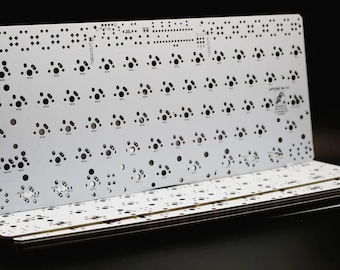 Puede incluir: Una placa de circuito impreso blanca para teclado mecánico, con una rejilla de orificios de montaje para interruptores y almohadillas de soldadura. La placa tiene un acabado blanco mate con marcas y texto en negro, incluyendo APY6000 Rev 1.0.