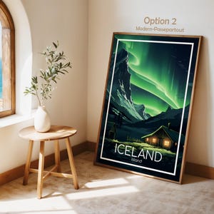 May include: A framed art print featuring a landscape of Iceland under the aurora borealis. The artwork showcases a cabin with lit windows, mountains, and the text "ICELAND Island" in white. The frame is brown.