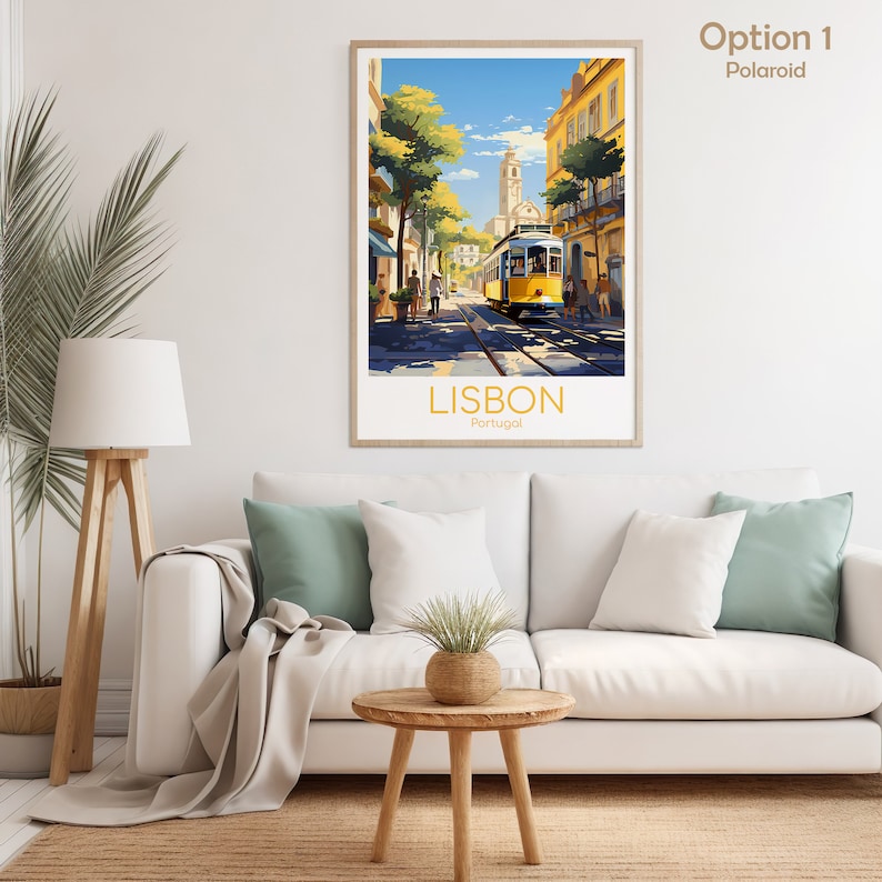 May include: A framed art print of Lisbon, Portugal, featuring a yellow tram on tracks in a sunlit street scene. The print has a light wooden frame and is displayed above a white sofa with green and white pillows. The text "LISBON Portugal" is at the bottom.