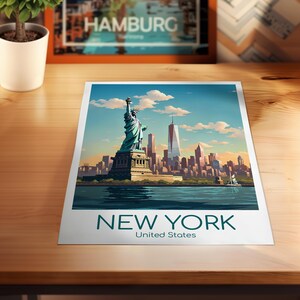 May include: A rectangular art print featuring a stylized illustration of the Statue of Liberty and the New York City skyline under a blue sky with clouds. The text NEW YORK United States is printed in dark teal at the bottom of the white border.