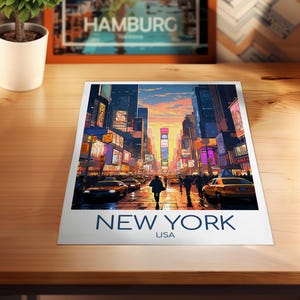 May include: A rectangular art print featuring a vibrant illustration of a New York City street scene at sunset, with yellow taxis, pedestrians, and glowing billboards. The text NEW YORK USA is printed in bold blue capital letters at the bottom.