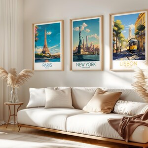 May include: Three framed travel posters hanging on a wall above a white sofa. The left poster shows the Eiffel Tower in Paris, the center poster depicts the Statue of Liberty in New York, and the right poster features a yellow tram in Lisbon.