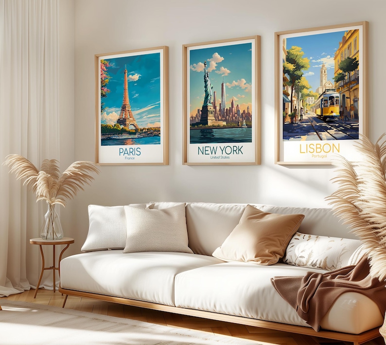 May include: Three framed travel posters hanging on a wall above a white sofa. The left poster shows the Eiffel Tower in Paris, the center poster depicts the Statue of Liberty in New York, and the right poster features a yellow tram in Lisbon.
