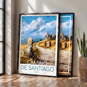 May include: A framed travel poster featuring a painted landscape of the Camino de Santiago in Spain. The artwork depicts two hikers on a dirt path leading toward a stone church under a blue sky with clouds. The text reads CAMINO DE SANTIAGO Spain.