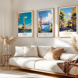 May include: Three framed travel art prints featuring iconic landmarks: the Eiffel Tower in Paris, the Golden Gate Bridge in San Francisco, and a street scene in Lisbon. Each print has a light wood frame and includes the city name.