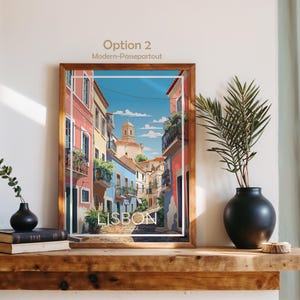 May include: A framed art print titled Lisbon, Portugal, featuring a colorful street scene with pink and blue buildings, balconies with plants, and a church tower under a blue sky. The print is displayed in a wooden frame on a wooden shelf.
