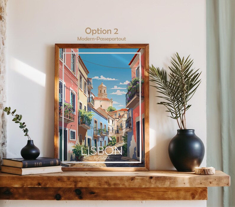 May include: A framed art print titled Lisbon, Portugal, featuring a colorful street scene with pink and blue buildings, balconies with plants, and a church tower under a blue sky. The print is displayed in a wooden frame on a wooden shelf.