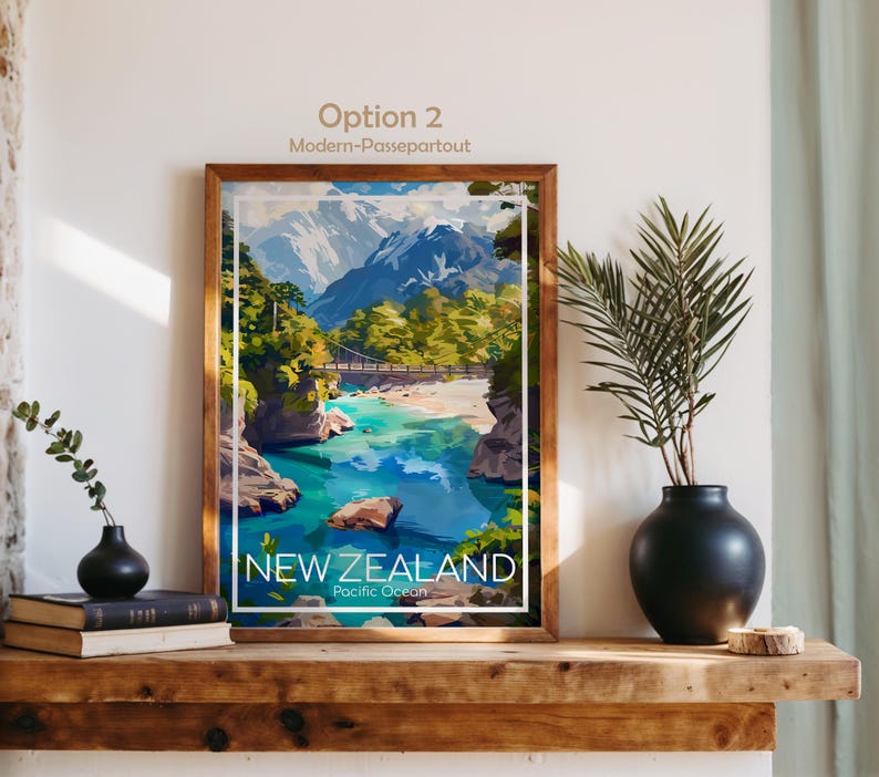 Puede incluir: Una l&aacute;mina art&iacute;stica enmarcada con una ilustraci&oacute;n paisaj&iacute;stica de Nueva Zelanda con monta&ntilde;as nevadas, un puente colgante sobre un r&iacute;o turquesa y &aacute;rboles verdes. El texto en la parte inferior dice NEW ZEALAND Pacific Ocean.