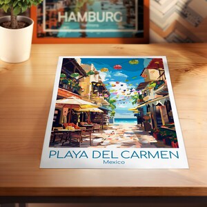 K&ouml;nnte beinhalten: Ein farbenfroher Druck von Playa Del Carmen, Mexiko, mit einer lebendigen Stra&szlig;enszene mit Gesch&auml;ften, Restaurants und Blick auf das Meer. Der Druck hat den Text "PLAYA DEL CARMEN Mexico" in blauer Schrift. Ein gerahmter Druck von Hamburg ist im Hintergrund.