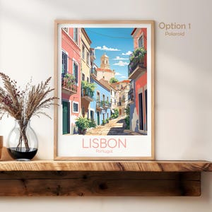 May include: A framed art print featuring a colorful street scene in Lisbon, Portugal. The illustration depicts narrow buildings in shades of pink, yellow, and blue with balconies, plants, and a church tower under a blue sky. The text reads LISBON Portugal.