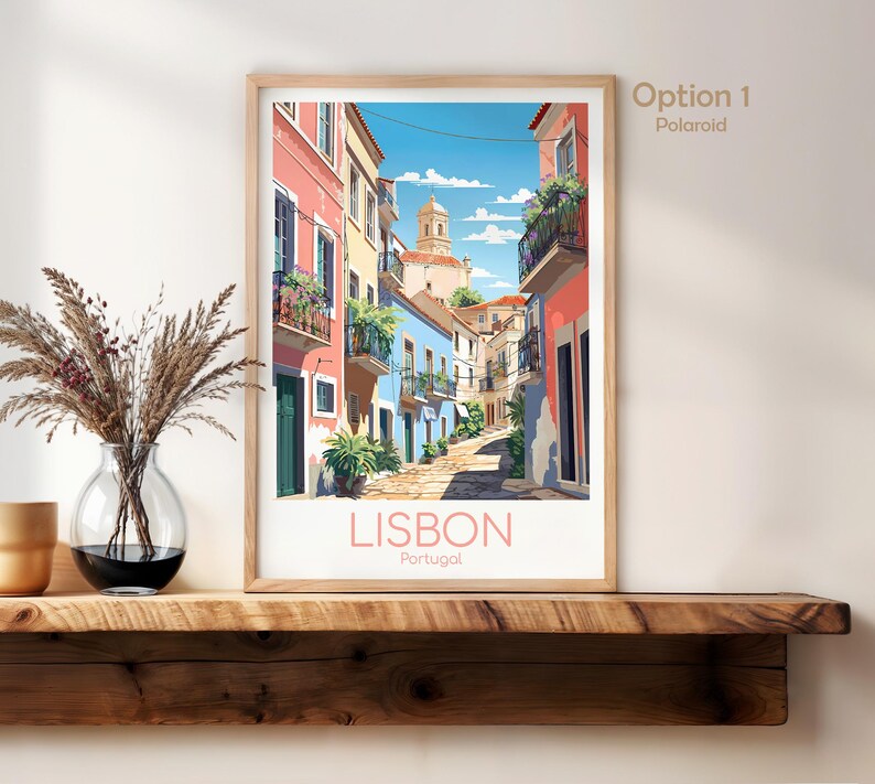 May include: A framed art print featuring a colorful street scene in Lisbon, Portugal. The illustration depicts narrow buildings in shades of pink, yellow, and blue with balconies, plants, and a church tower under a blue sky. The text reads LISBON Portugal.
