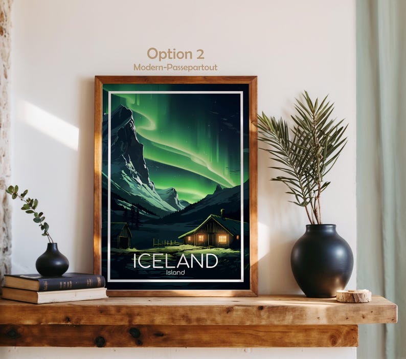 May include: A framed print of Iceland's landscape, featuring the Northern Lights. The artwork showcases a cabin with lit windows, mountains, and the text "ICELAND Island". The frame is a warm brown color.