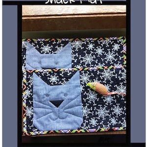 Può includere: Due tovagliette trapuntate rettangolari con un'applicazione a forma di muso di gatto azzurro su sfondo nero con motivo a ragnatela bianca. Le tovagliette presentano un bordo a zigzag arancione, viola e verde e un topo in tessuto.