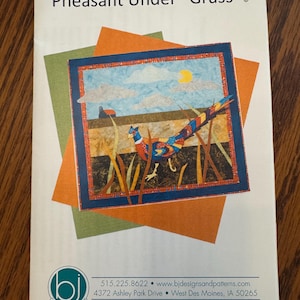 May include: A brochure titled "Pheasant Under 'Grass'" featuring a colorful quilt design. The quilt depicts a pheasant in a field with a blue sky and a yellow sun. The brochure includes contact information for "bj designs and patterns."