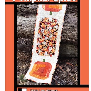 May include: A quilted table runner with a pumpkin spice theme. The runner features pumpkin shapes and a central panel with a pumpkin and leaf pattern. The text "Pumpkin Spice" is at the top. Designed by Tricia Lynn Maloney.