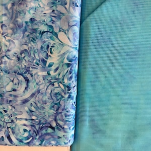 May include: Two fabric samples. One is a roll of fabric with a blue and white floral pattern. The other is a flat piece of turquoise fabric with a grid pattern. Both fabrics have a watercolor effect.