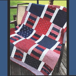 May include: A patchwork quilt in red, white, and blue, draped over a wooden chair. The quilt features various patterns, including floral and striped designs. The text "1776" is at the top. The quilt is a patriotic theme.