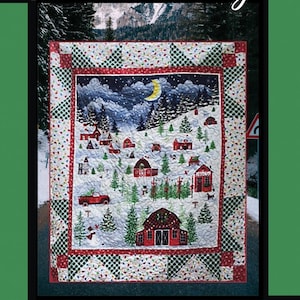 Może przedstawiać: Kołdra z zimową scenerią przedstawiającą czerwone domy, ośnieżone drzewa i półksiężyc. Kołdra ma wzorzystą obwódkę i napis "Homecoming" u góry. Zaprojektowany przez Tricia Lynn Maloney.