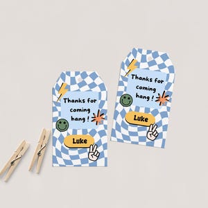 Könnte beinhalten: Zwei Geschenkanhänger mit blau-weißem Karomuster. Jeder Anhänger hat den Text "Thanks for coming hang!" und den Namen "Luke". Dekorative Elemente sind ein Smiley, ein Blitz und ein Friedenszeichen.