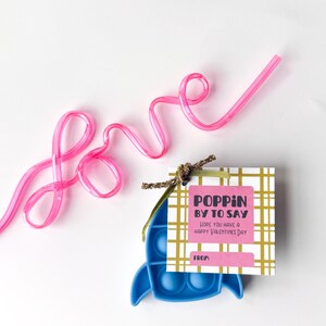 May include: A Valentine's Day gift set featuring a blue pop-it toy, a pink straw spelling "love", and a gift tag that reads "Poppin' by to say, Hope you have a Happy Valentine's Day."