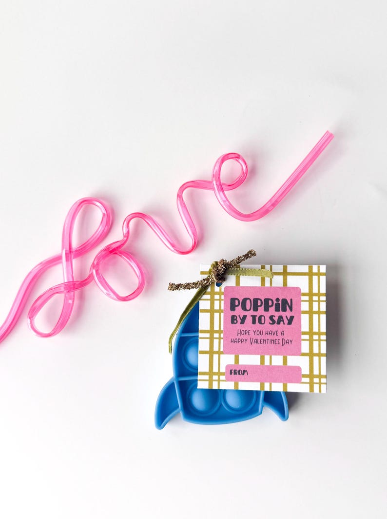 May include: A Valentine's Day gift set featuring a blue pop-it toy, a pink straw spelling "love", and a gift tag that reads "Poppin' by to say, Hope you have a Happy Valentine's Day."