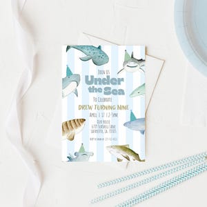 Op de afbeelding: Een verjaardagsuitnodiging met een blauw-wit gestreepte achtergrond en illustraties van haaien. De tekst luidt "Under the Sea" en nodigt gasten uit om Drews negende verjaardag te vieren.
