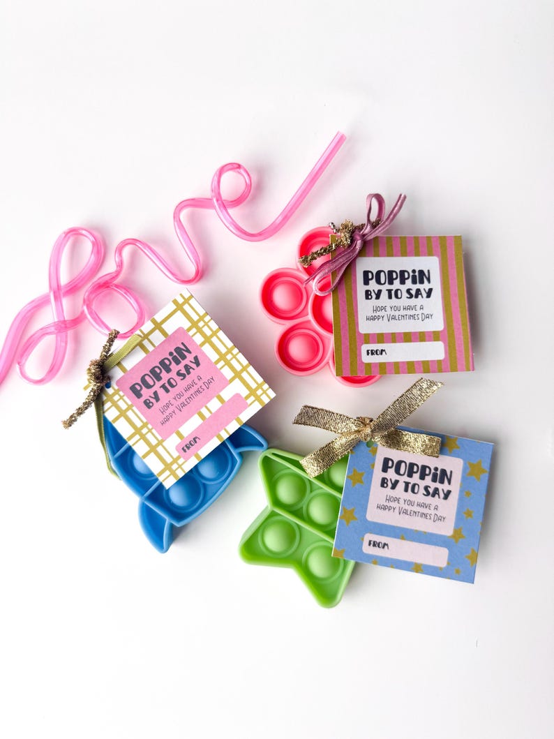 May include: Valentine's Day gifts featuring colorful pop-it toys in blue, green, and pink, each with a tag that reads "Poppin' by to say, hope you have a happy Valentine's Day." A pink straw spells out "love".