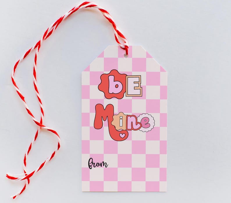 May include: Pink and white checkered gift tag with the text "Be Mine" in red and pink letters. The tag has a red and white twine string attached to it. The tag also has the word "from" written in black at the bottom.